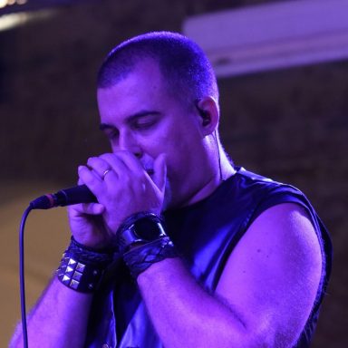Uomo che canta al microfono, indossando una giacca nera, con espressione intensa.