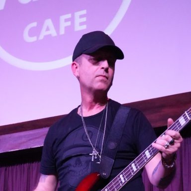 Music performer playing bass guitar on stage with purple lighting.