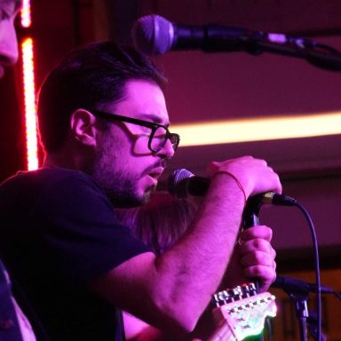 Music artist singing into a microphone on stage, wearing glasses and focused on performance.