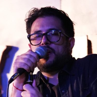 Music artist singing into a microphone on stage, wearing glasses and focused on performance.